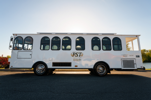 A sleek, white trolley from PST Trolley parked outdoors with the company logo and contact information displayed on the side.