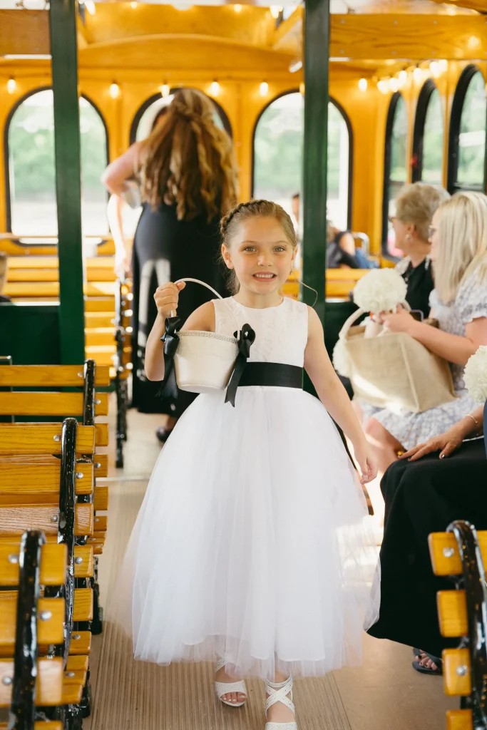 A little girl dressed in a white dress with a black bow, radiating happiness in a bright, cheerful environment at PST Trolley