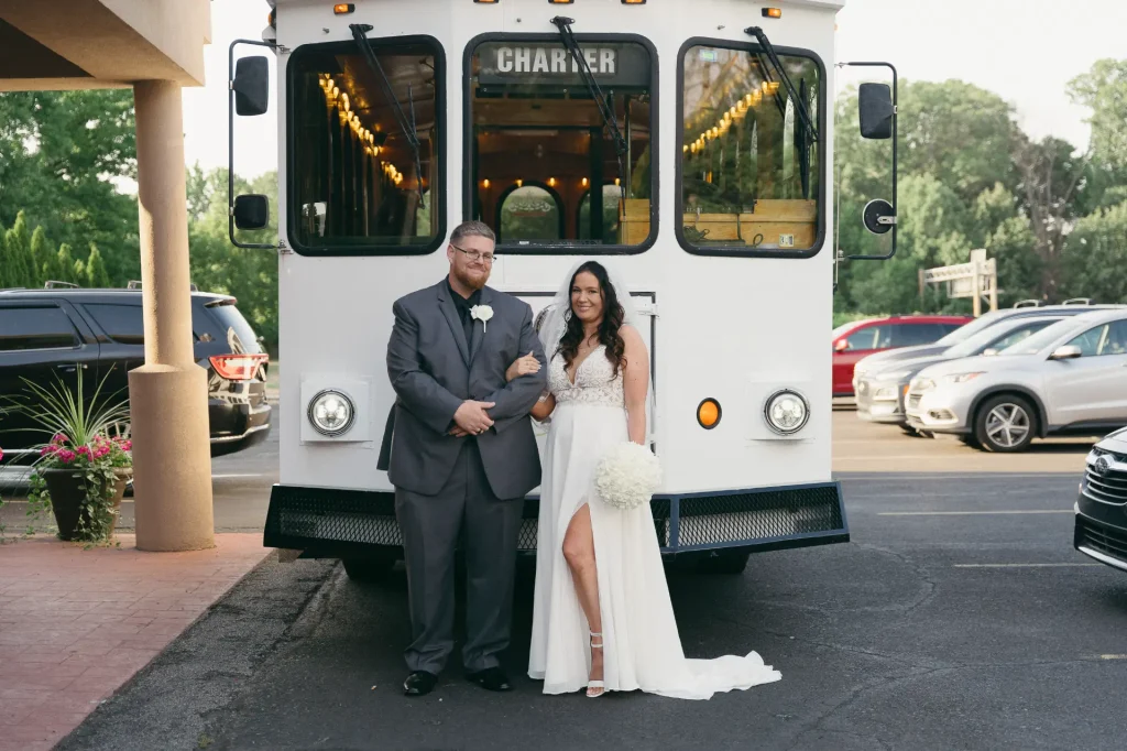 A joyful bride and groom pose in front of a classic trolley, symbolizing their union on this special occasion at PST Trolley