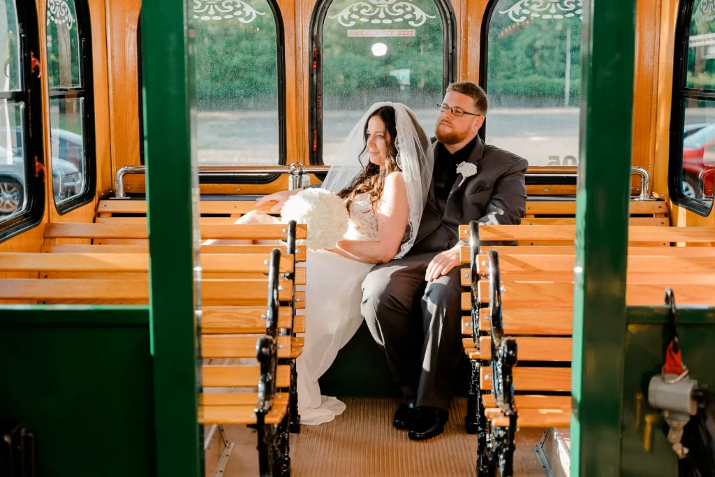 A bride and groom joyfully seated on the back of a trolley, celebrating their special day.