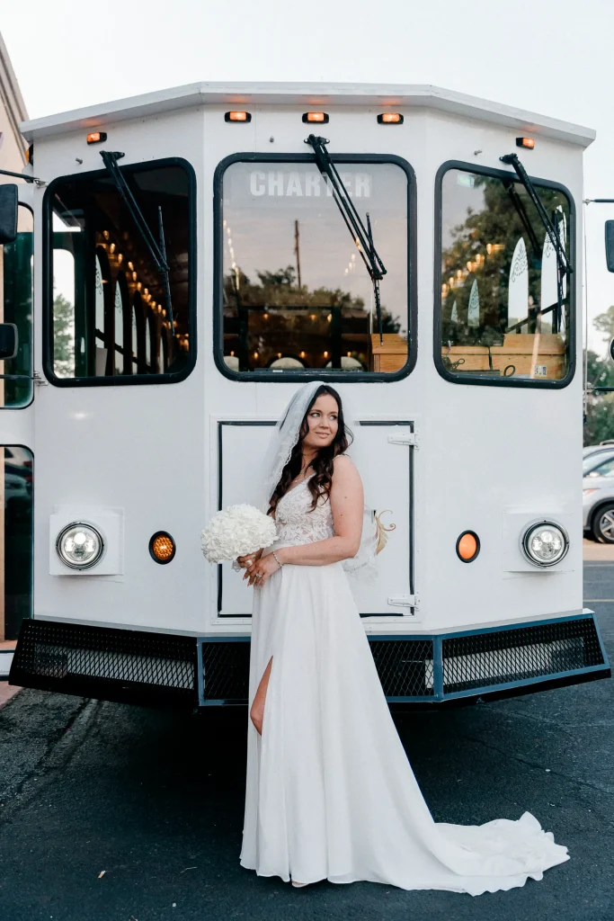 A bride poses for a photograph beside a classic white trolley, showcasing her stunning attire in PST Trolley